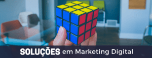 A imagem apresenta em primeiro plano a fotografia de uma mão segurando um cubo mágico montado. No rodapé, lemos a frase: Soluções em Marketing Digital.